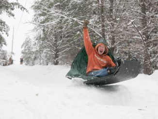 boy raising fist as he sleds over snow ramp