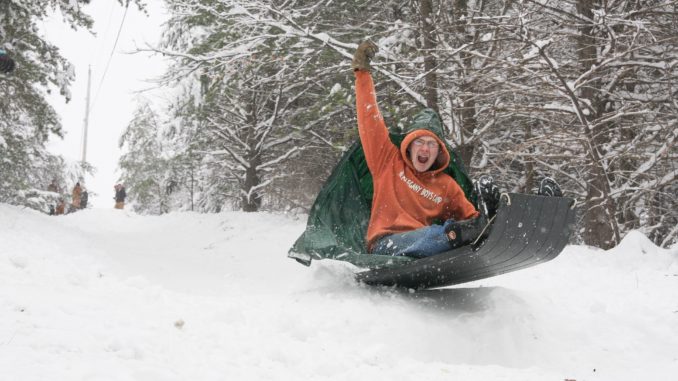 boy raising fist as he sleds over snow ramp